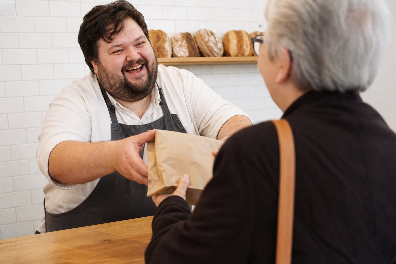 Baker handing a paper bag across the counter to his first customer
